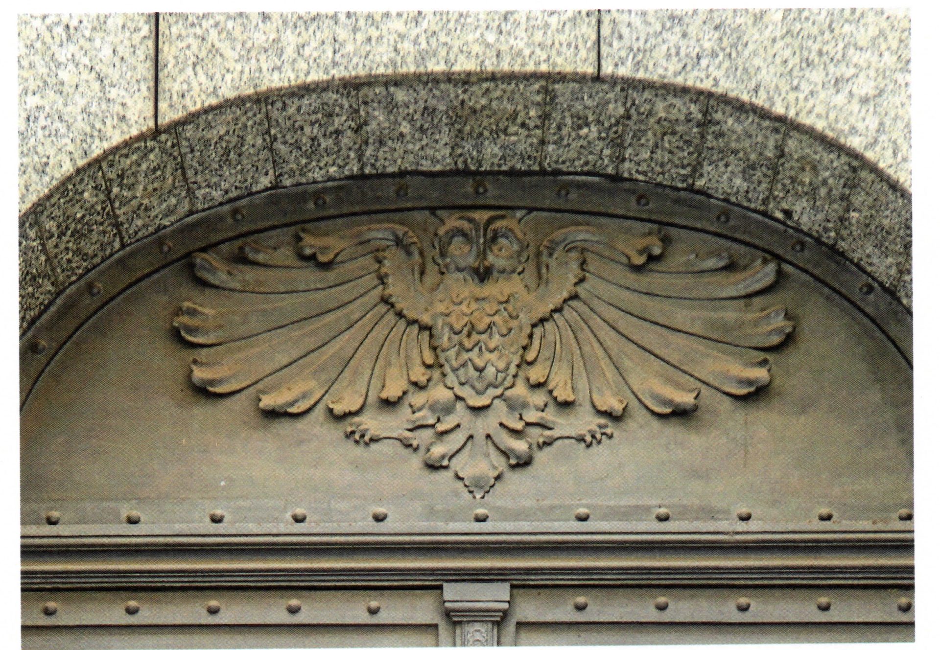 Nahaufnahme des Tympanons über der eisernen Pforte der Allmutterburg in Prag: ein Uhu mit weit ausgebreiteten Schwingen, in Bronze getrieben, darüber ein Bogen aus Granitquadern